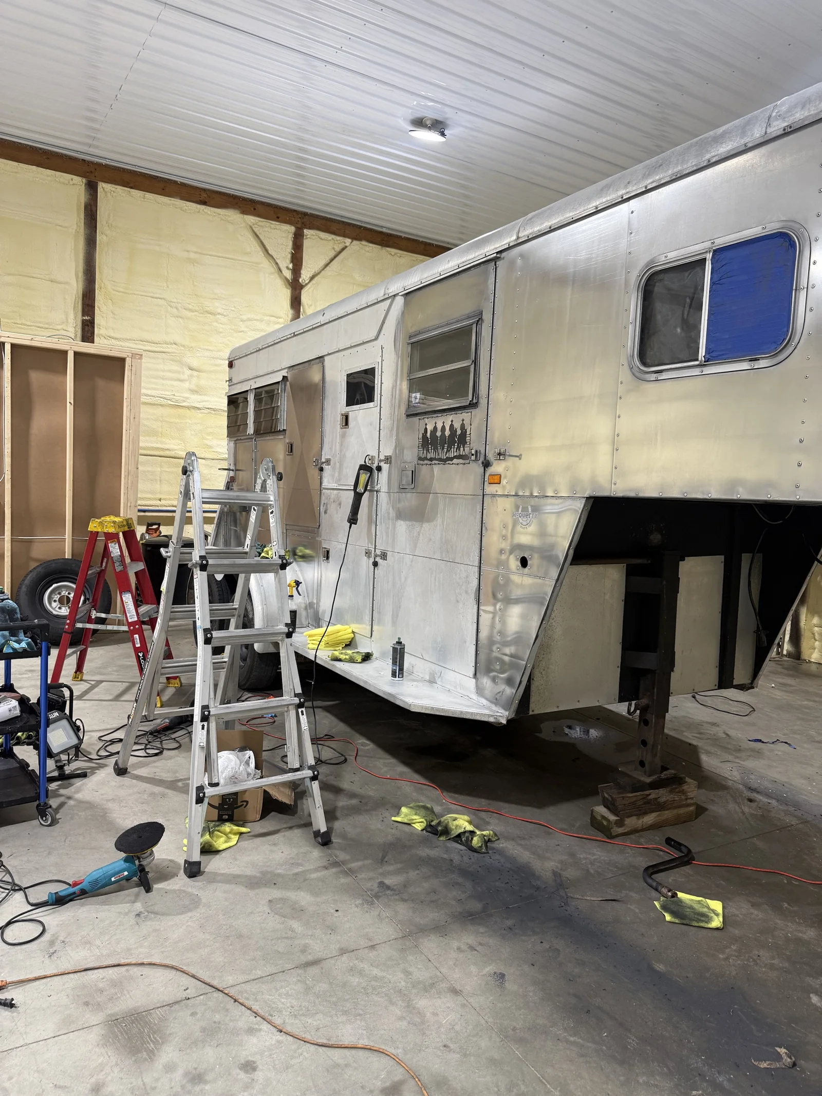 Aluminum horse trailer mid-polish in the shop, with ladders and polishers set up