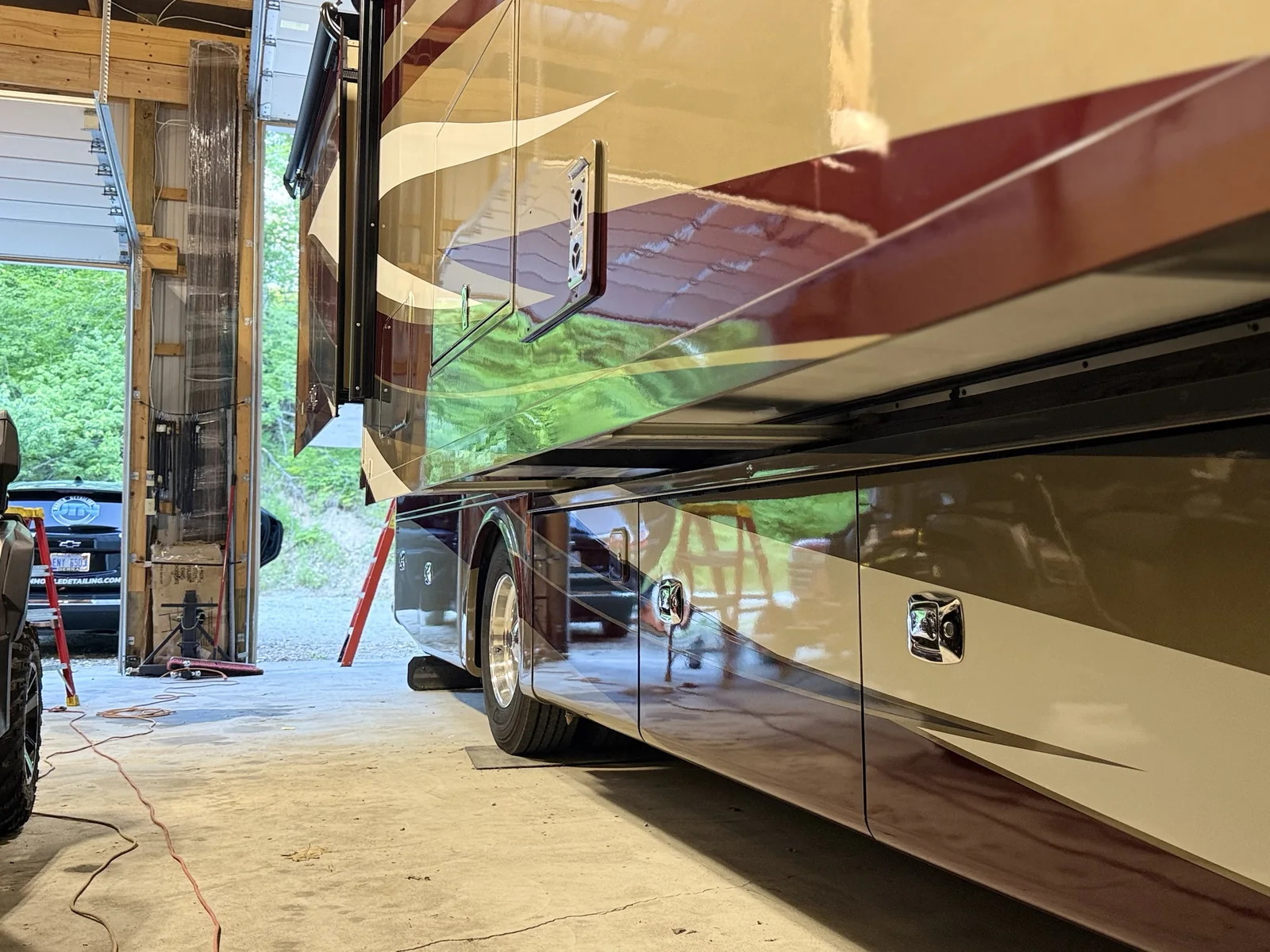 Glossy lower panels and compartment doors on a Class A motorhome after detailing, JTN unit in the background