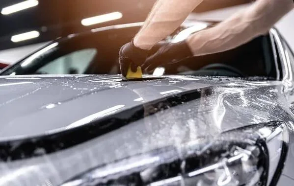 Installer squeegeeing clear paint protection film across a silver car's hood