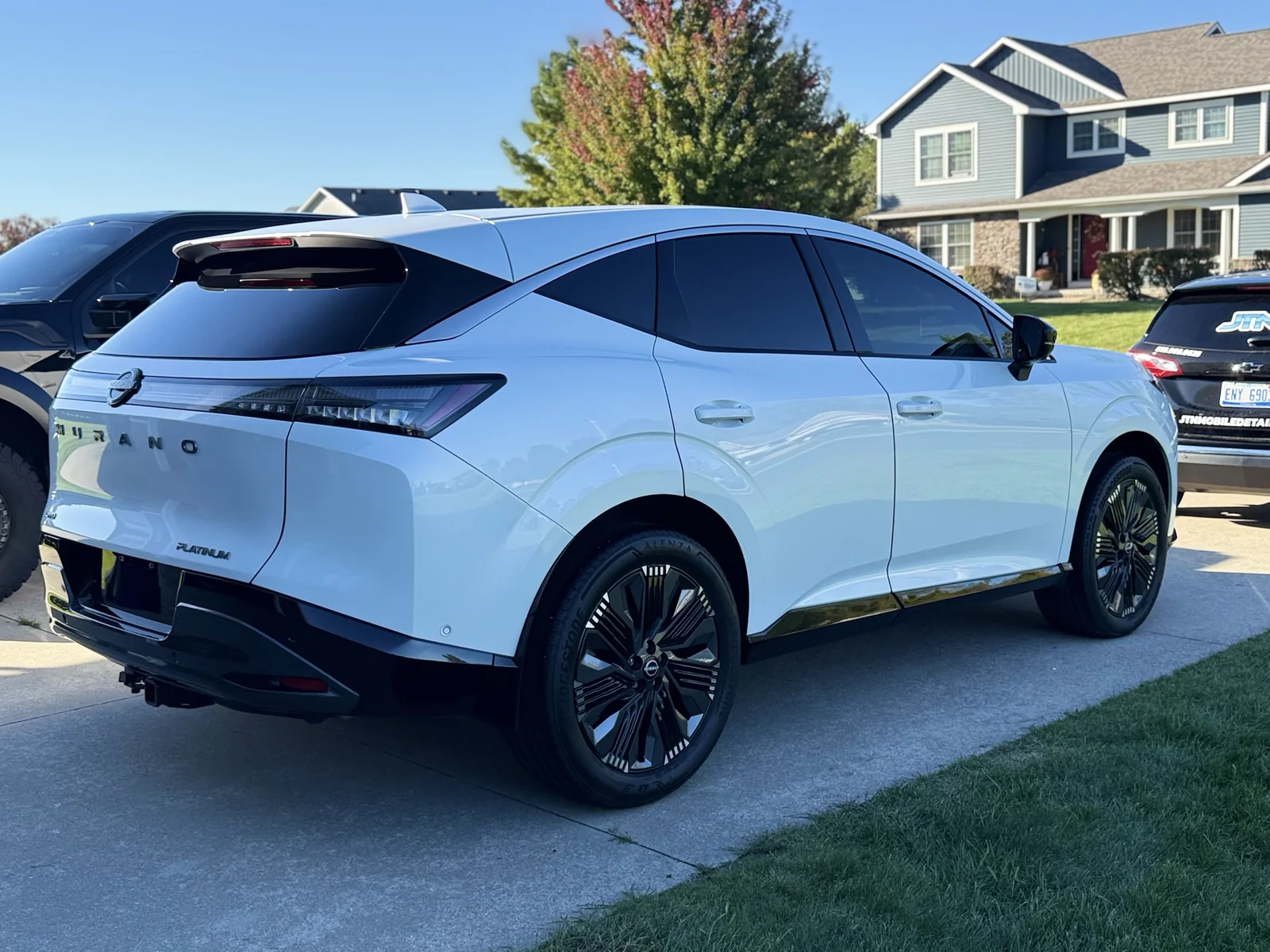 White Nissan Murano after a driveway mobile detail, with a JTN Mobile Detailing unit parked alongside